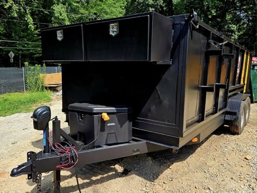 A black dump trailer with toolboxes parked on a gravel yard, ready for a haul-away.